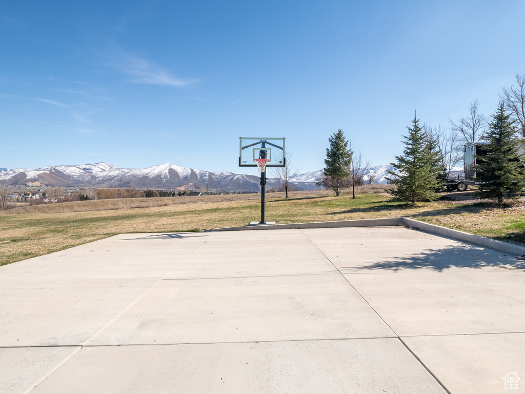 View of sport court featuring a mountain view, a lawn, and basketball hoop