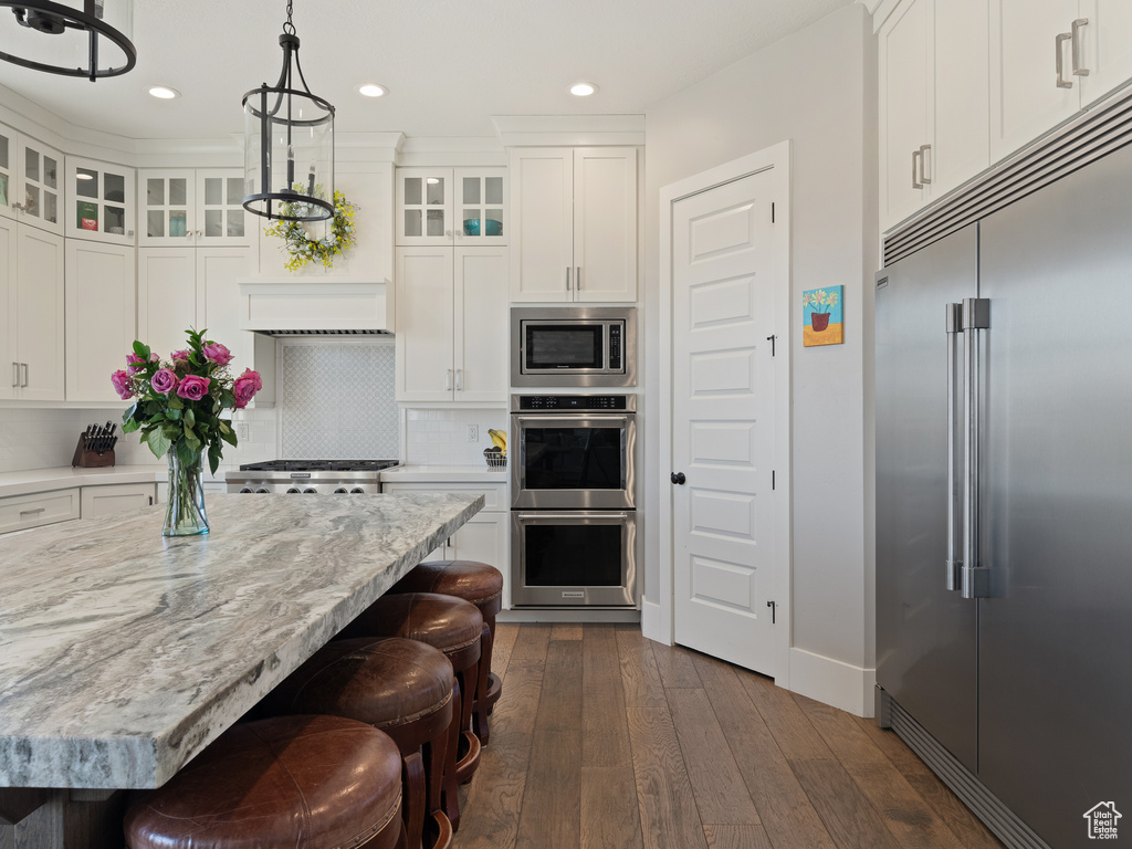 Kitchen featuring a kitchen breakfast bar, white cabinetry, built in appliances, dark wood-style floors, and recessed lighting