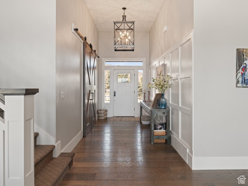 Entrance foyer with a barn door, baseboards, dark wood-style flooring, a towering ceiling, and stairs