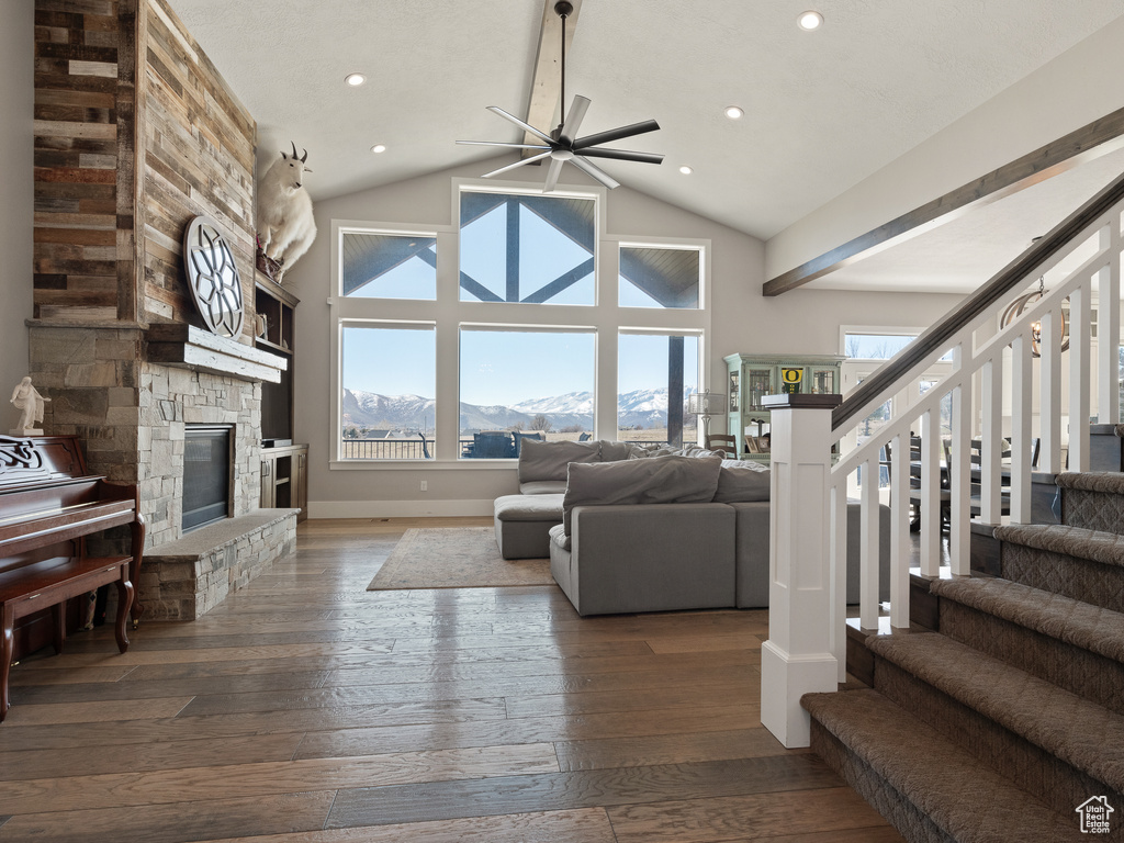 Living area featuring hardwood / wood-style flooring, ceiling fan, a fireplace, stairway, and high vaulted ceiling