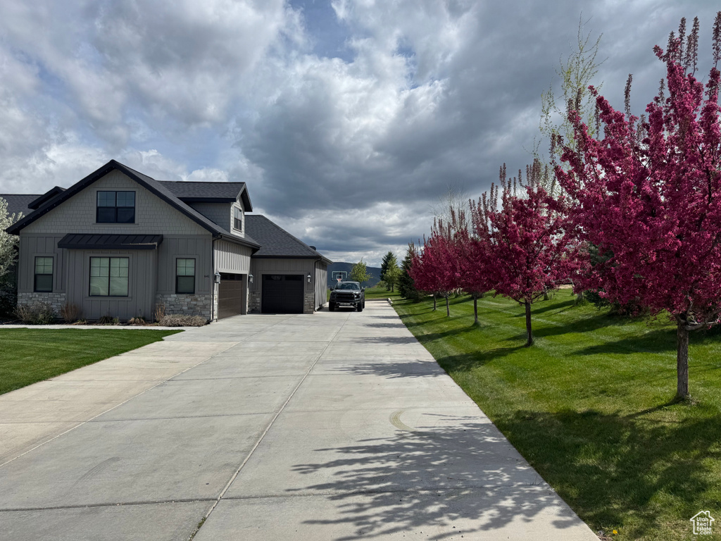 View of front of home with an attached garage, board and batten siding, stone siding, driveway, and a front yard