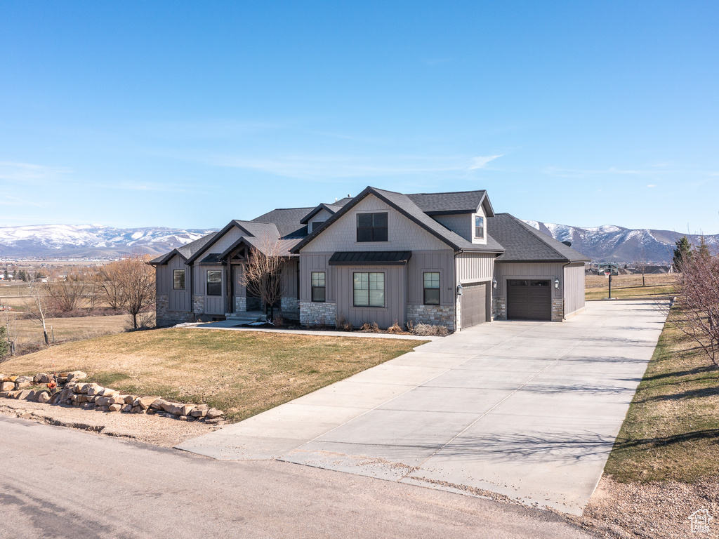 Modern inspired farmhouse with a front lawn, a garage, a mountain view, stone siding, and board and batten siding