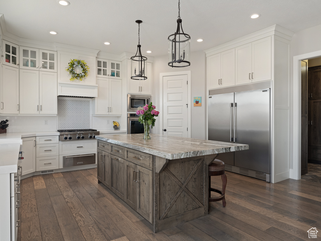 Kitchen with built in appliances, light countertops, white cabinets, and a center island