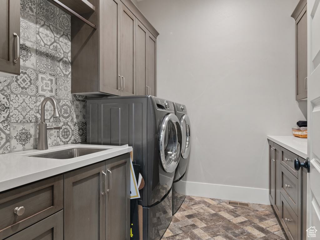 Washroom with a sink, cabinet space, baseboards, washer and dryer, and brick floor