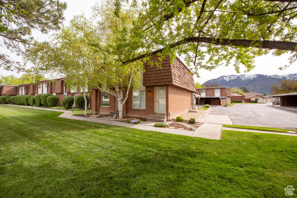 View of front of property with a front yard, a mountain view, brick siding, entry steps, and mansard roof