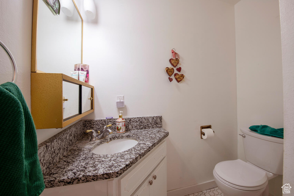 Half bathroom with baseboards, tile patterned floors, toilet, and vanity
