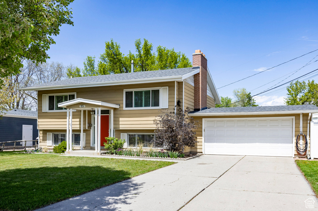 Bi-level home with concrete driveway, a chimney, roof with shingles, a front yard, and a garage