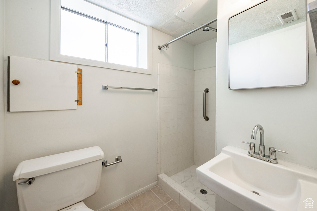 Bathroom with tile patterned floors, a tile shower, toilet, and a sink