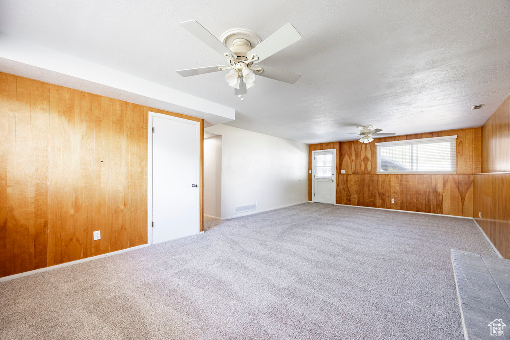Unfurnished room with wooden walls, a ceiling fan, visible vents, and carpet