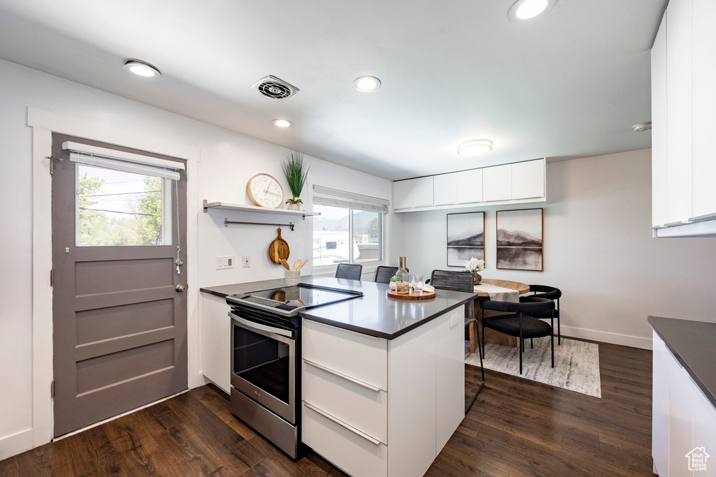 Kitchen with dark wood-style floors, stainless steel electric stove, dark countertops, and a peninsula