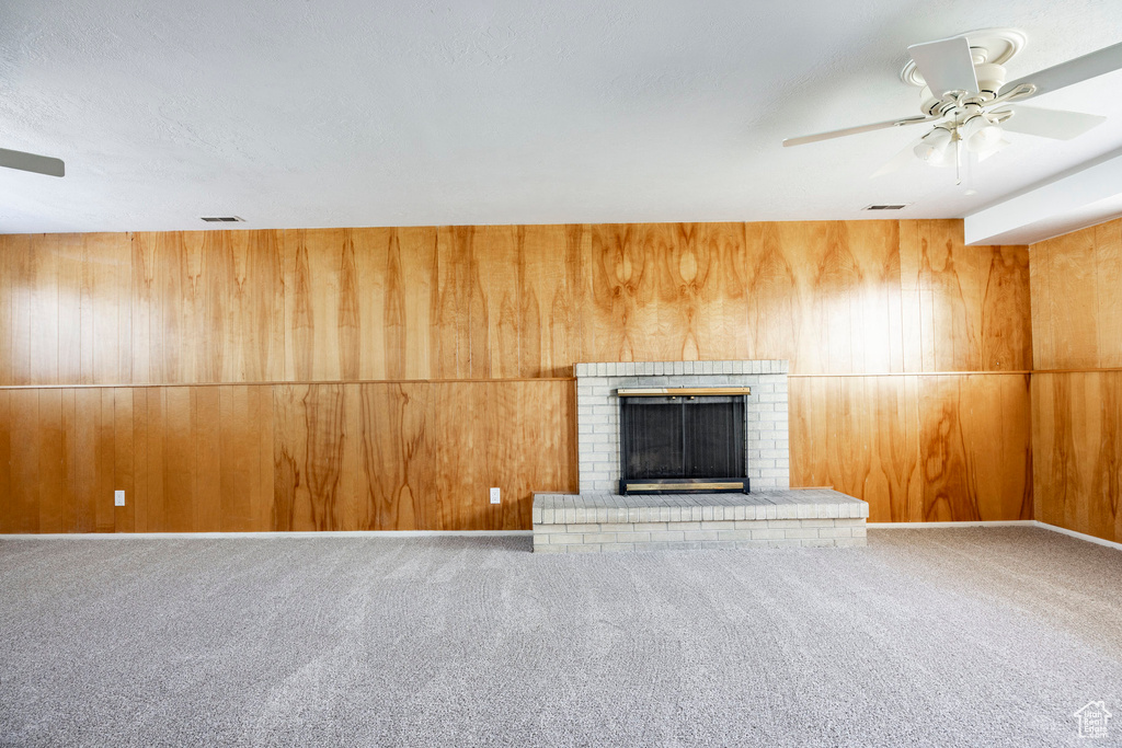 Unfurnished living room with wood walls, ceiling fan, carpet flooring, and a brick fireplace
