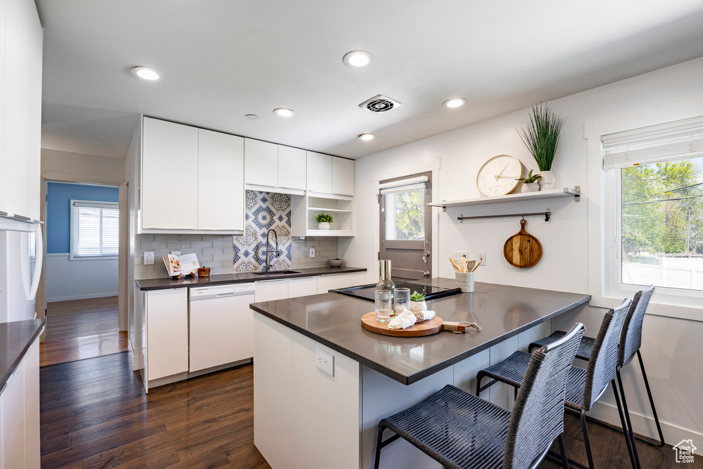 Kitchen featuring a sink, white dishwasher, open shelves, cooktop, and dark countertops