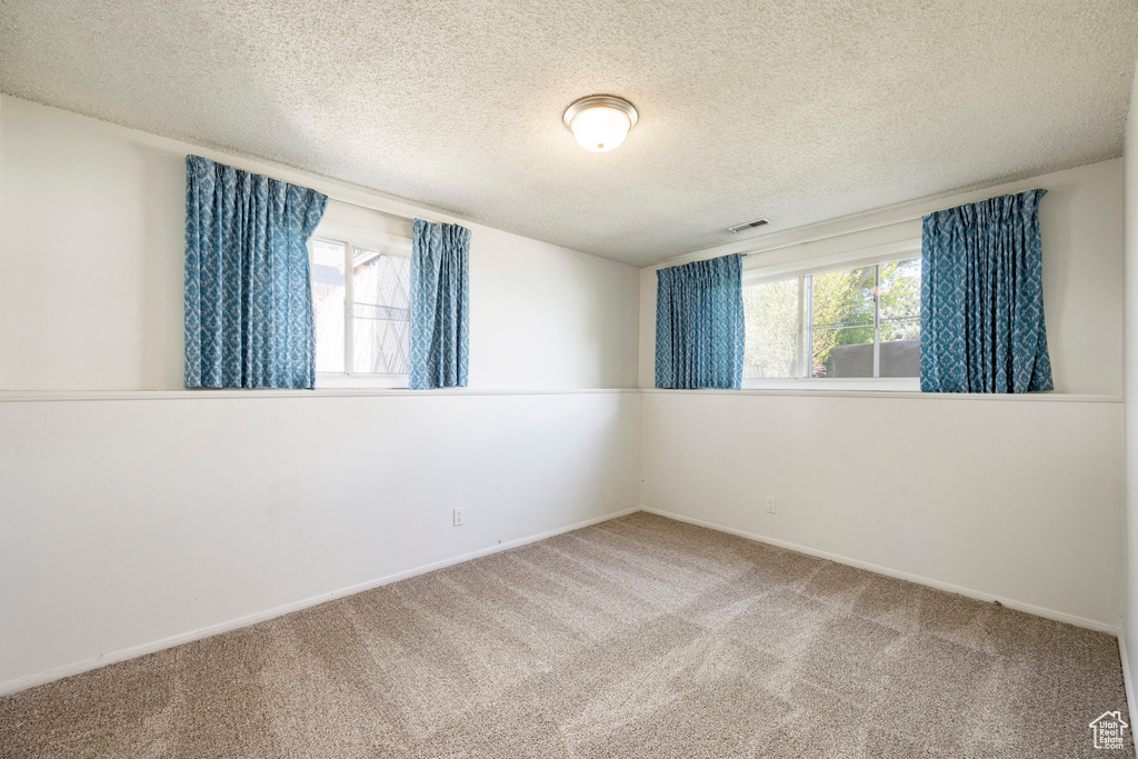 Carpeted spare room with a textured ceiling, visible vents, and baseboards