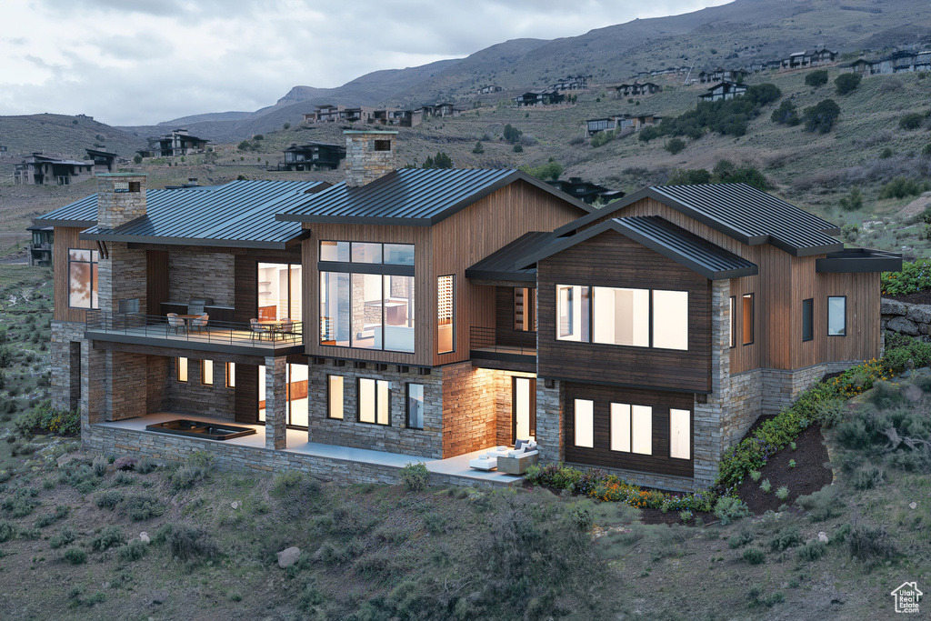 Rear view of house featuring stone siding, a mountain view, a standing seam roof, a chimney, and metal roof