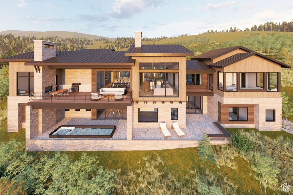 Rear view of property featuring a patio, a standing seam roof, a chimney, and stone siding