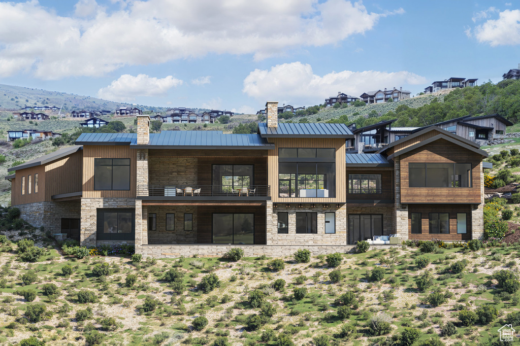 Back of property with a chimney, a balcony, and stone siding