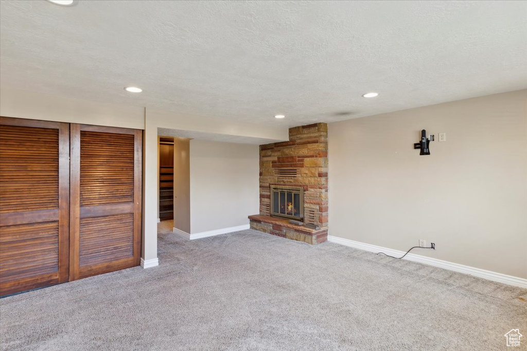 Unfurnished living room featuring recessed lighting, baseboards, a stone fireplace, and carpet