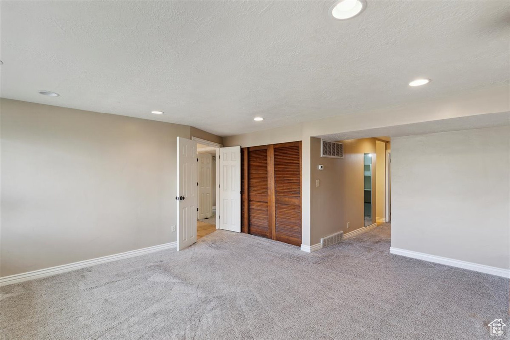 Unfurnished room featuring visible vents, a textured ceiling, and light carpet