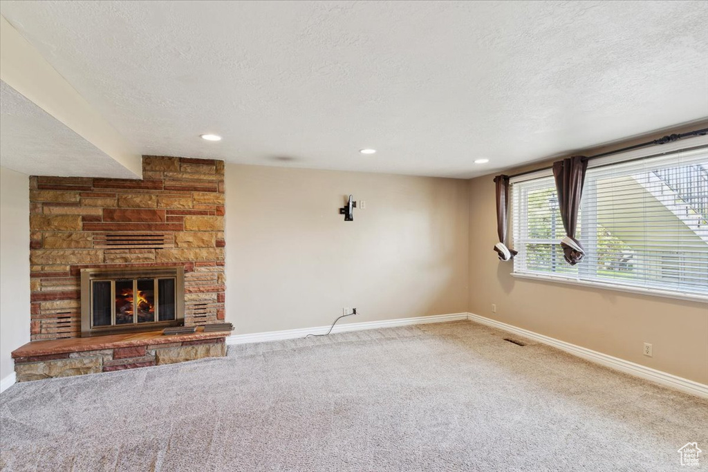 Unfurnished living room featuring baseboards, carpet flooring, a textured ceiling, and a fireplace