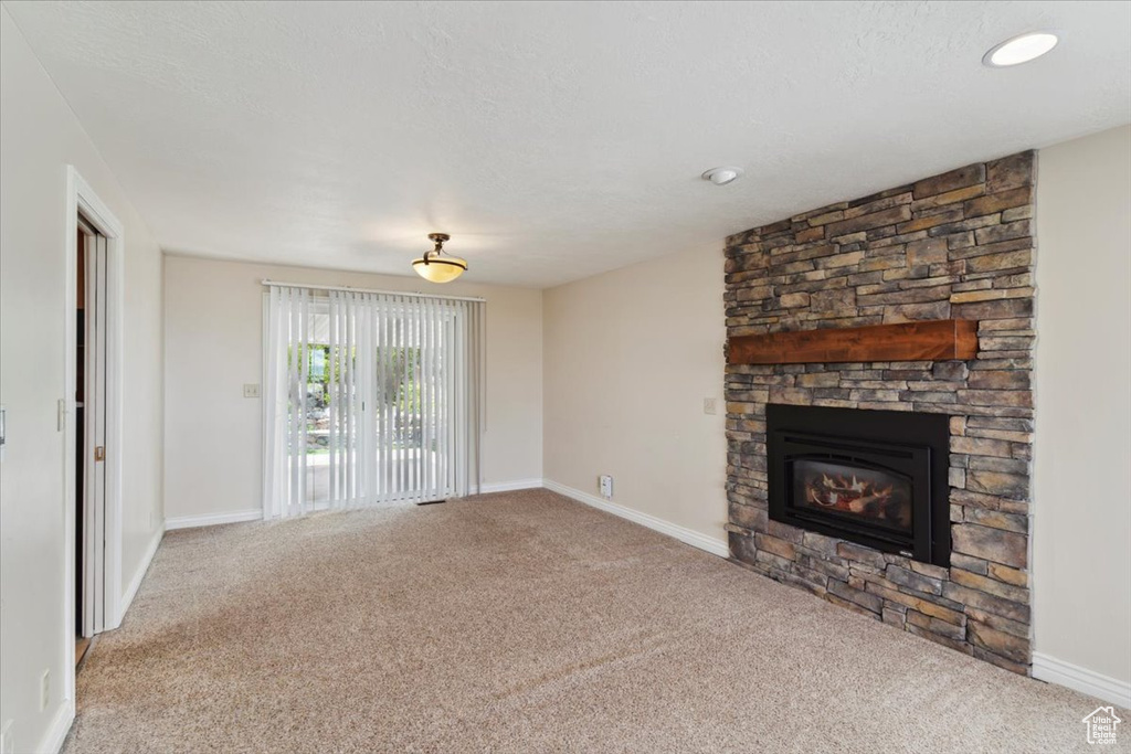 Unfurnished living room with baseboards, carpet flooring, and a stone fireplace