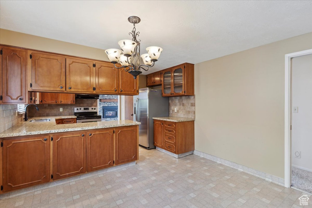 Kitchen featuring under cabinet range hood, a chandelier, brown cabinets, a sink, and appliances with stainless steel finishes