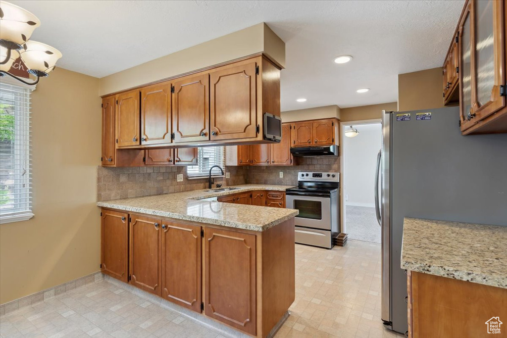 Kitchen featuring brown cabinetry, appliances with stainless steel finishes, a sink, a peninsula, and under cabinet range hood