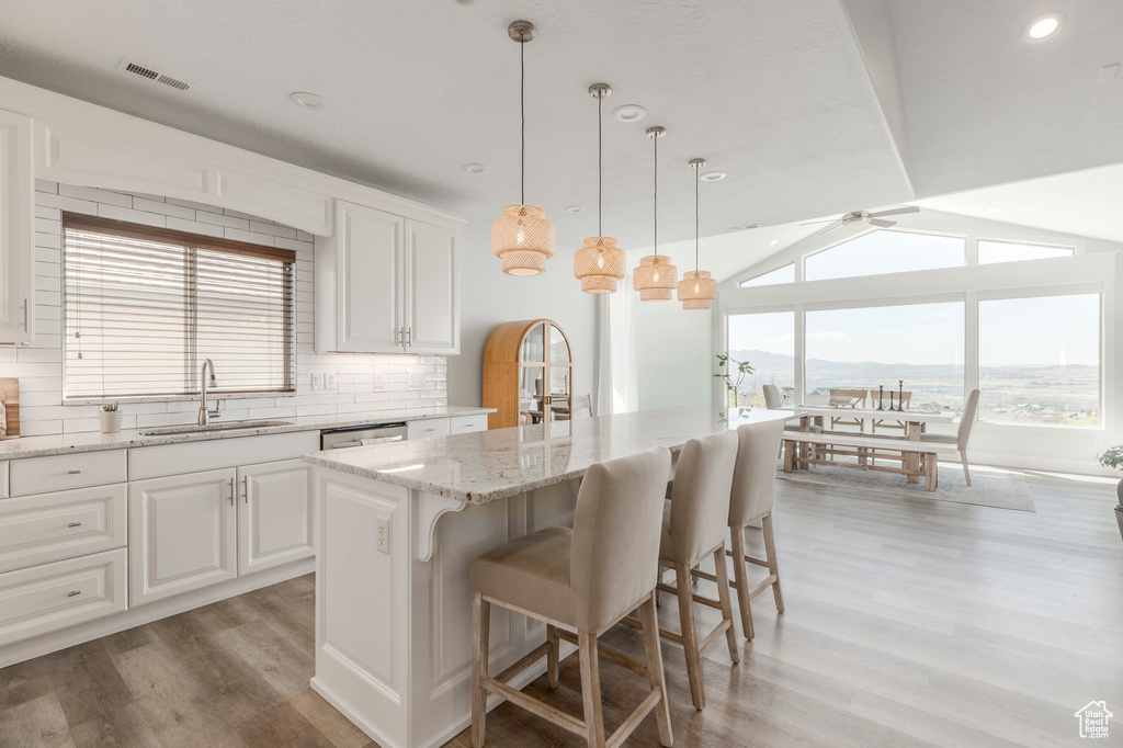 Kitchen with a sink, decorative backsplash, light wood-type flooring, a center island, and visible vents