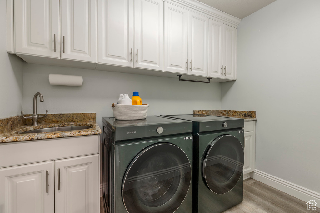 Laundry area featuring a sink, washing machine and dryer, baseboards, light wood finished floors, and cabinet space