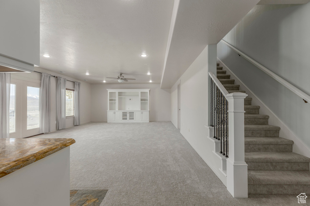 Unfurnished living room with stairway, ceiling fan, recessed lighting, and light carpet
