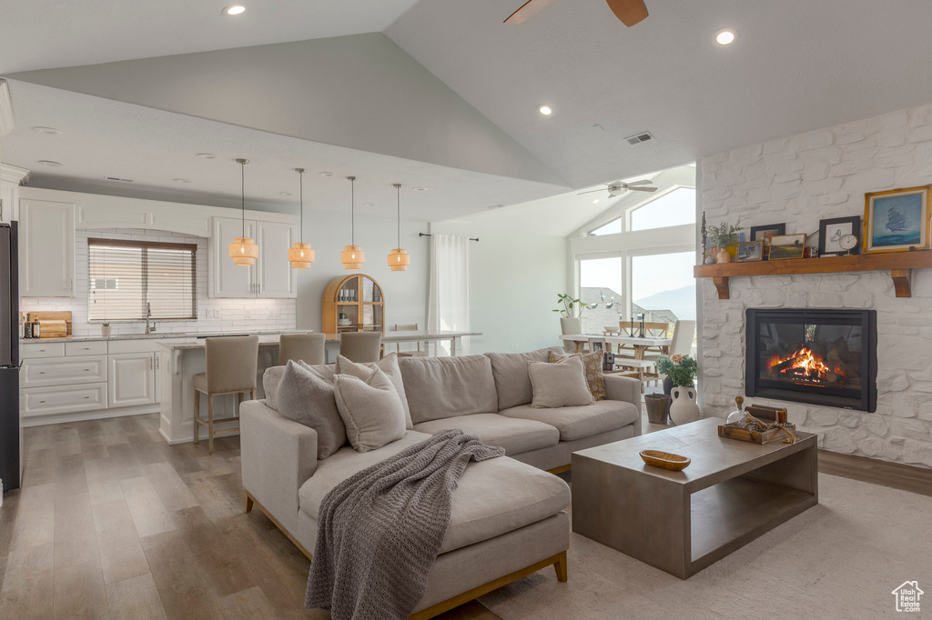 Living room with ceiling fan, high vaulted ceiling, light wood finished floors, and a stone fireplace
