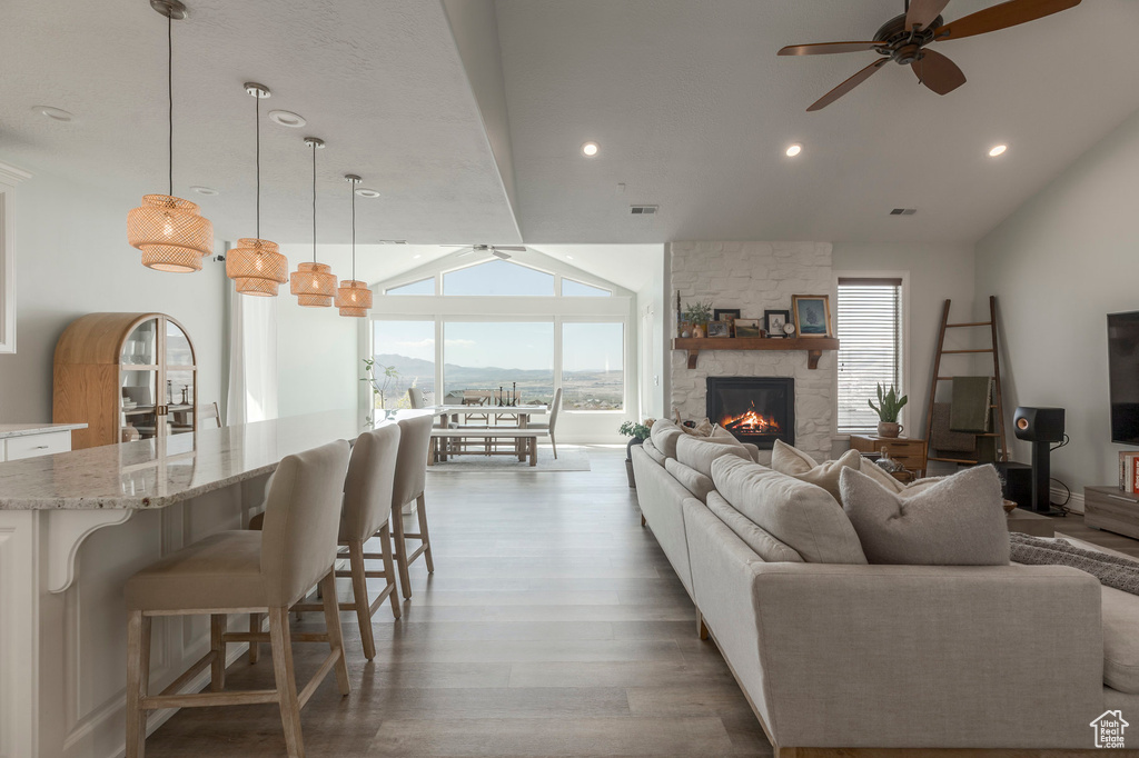 Living area with a ceiling fan, a stone fireplace, wood finished floors, and lofted ceiling