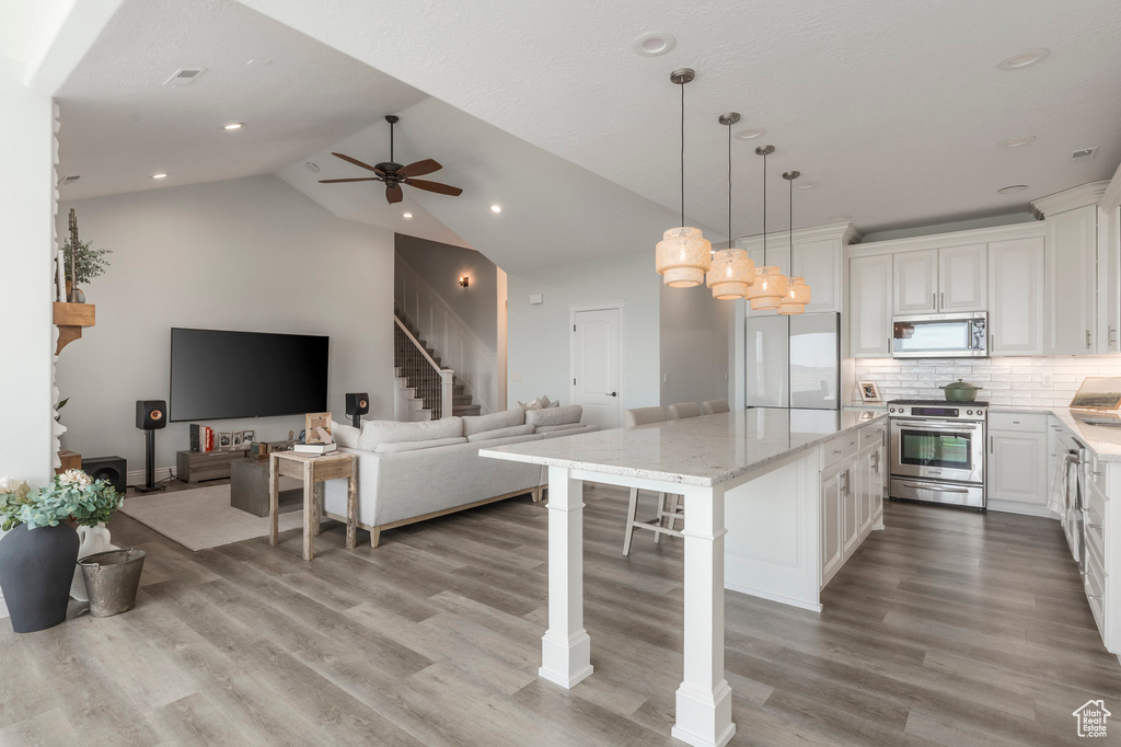 Kitchen with white cabinetry, appliances with stainless steel finishes, ceiling fan, a kitchen island, and light wood finished floors