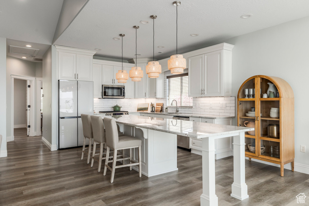 Kitchen featuring dark wood finished floors, a center island, appliances with stainless steel finishes, and tasteful backsplash