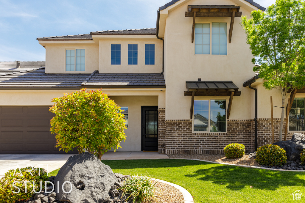 View of front of home with stucco siding, concrete driveway, brick siding, and a front lawn