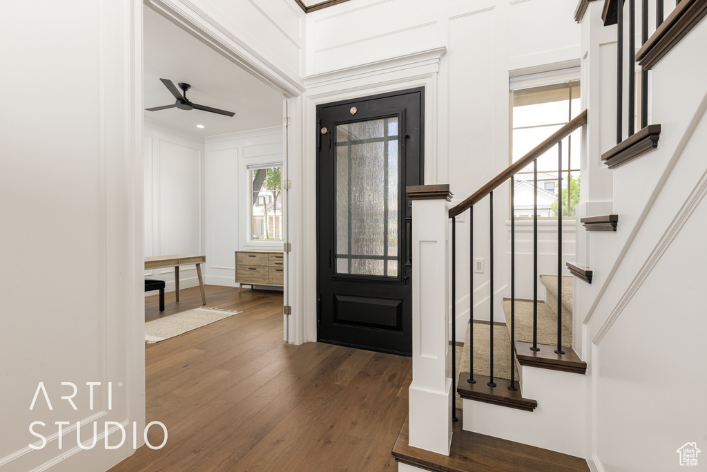 Foyer entrance with stairs, a decorative wall, ornamental molding, dark wood-style floors, and a ceiling fan