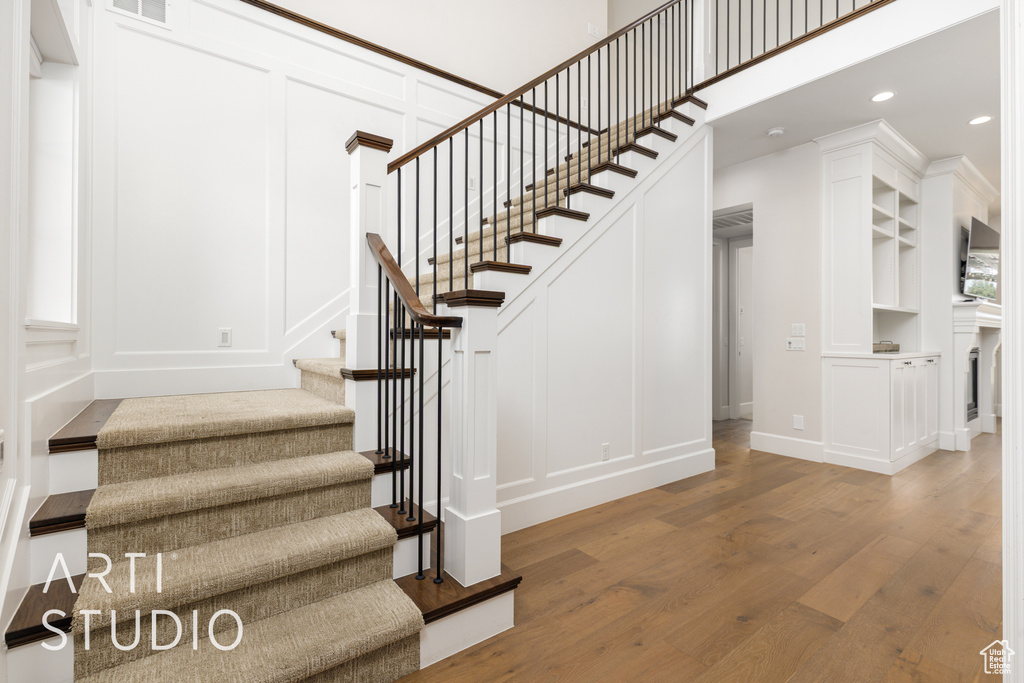 Stairway with recessed lighting, visible vents, a decorative wall, baseboards, and wood finished floors