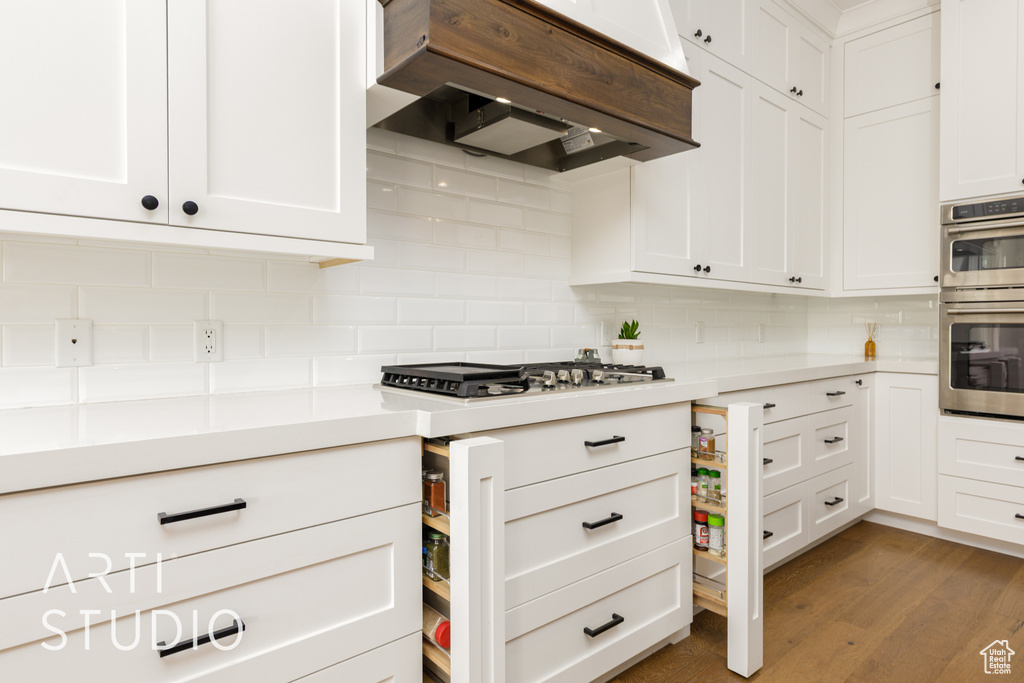 Kitchen with tasteful backsplash, white cabinetry, stainless steel appliances, light countertops, and ventilation hood