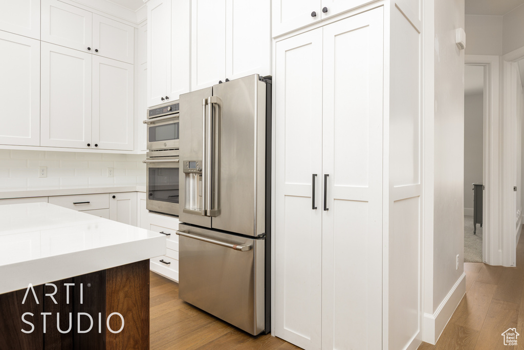 Kitchen featuring appliances with stainless steel finishes, white cabinetry, light wood-type flooring, and light countertops