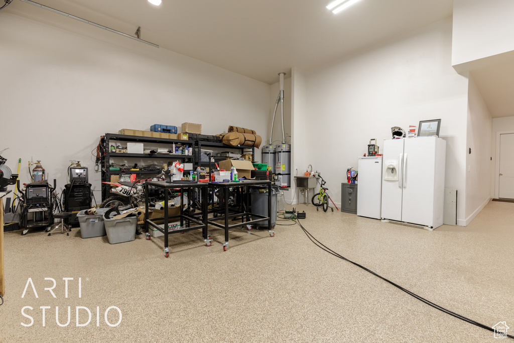 Garage featuring white refrigerator with ice dispenser, refrigerator, and strapped water heater