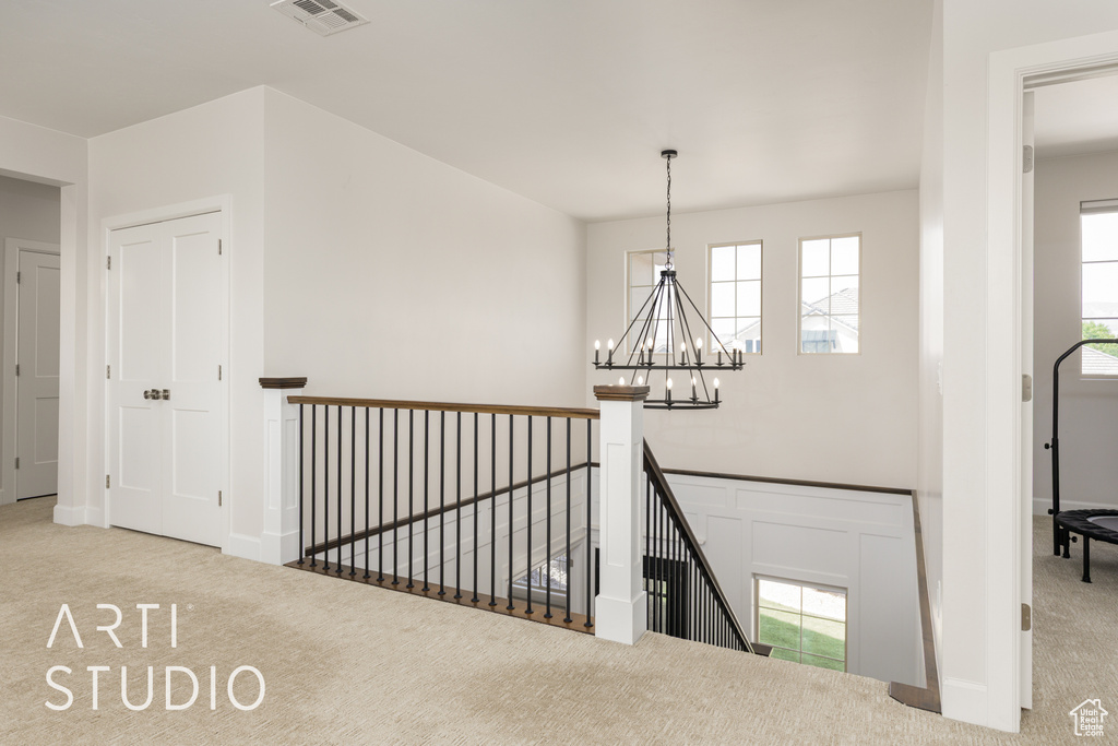 Hallway featuring an upstairs landing, carpet, visible vents, and a notable chandelier