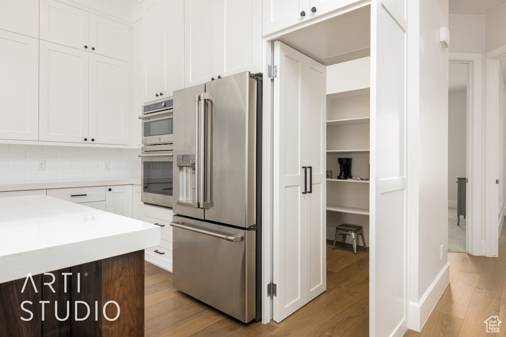 Kitchen with white cabinetry, wood finished floors, appliances with stainless steel finishes, and light countertops