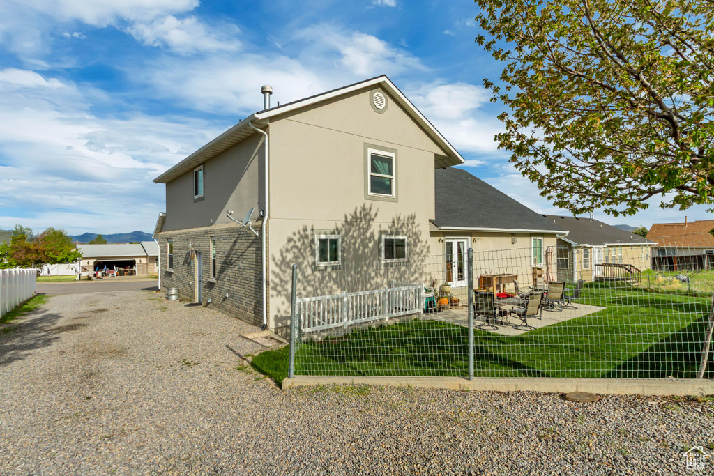 Back of property featuring stucco siding, brick siding, fence, a patio area, and a lawn