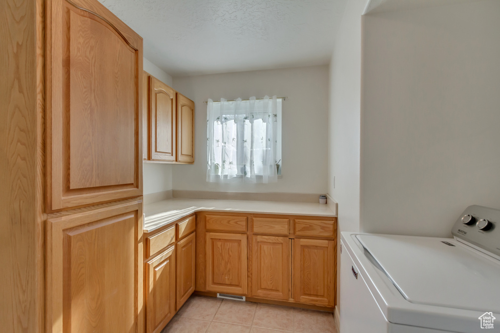Laundry area featuring light tile patterned floors, a textured ceiling, washer / clothes dryer, visible vents, and cabinet space
