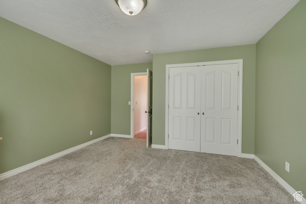 Unfurnished bedroom featuring carpet, baseboards, a textured ceiling, and a closet