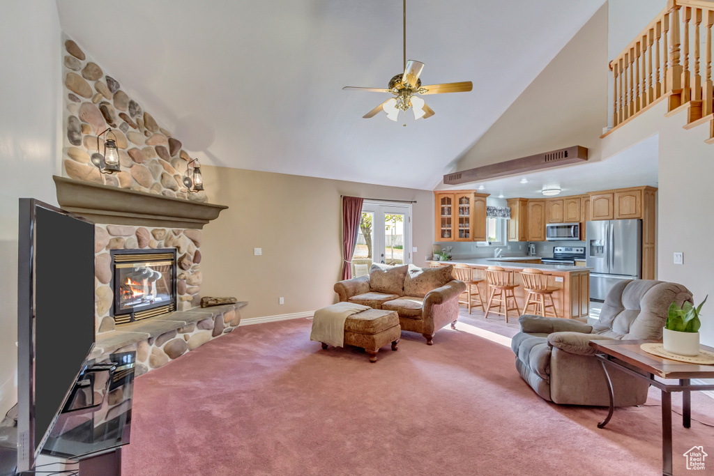 Living area with light carpet, ceiling fan, a fireplace, baseboards, and high vaulted ceiling