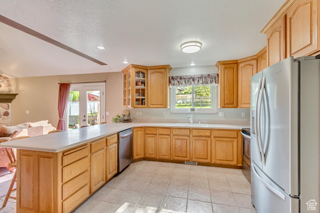 Kitchen with glass insert cabinets, a sink, stainless steel appliances, light countertops, and a peninsula