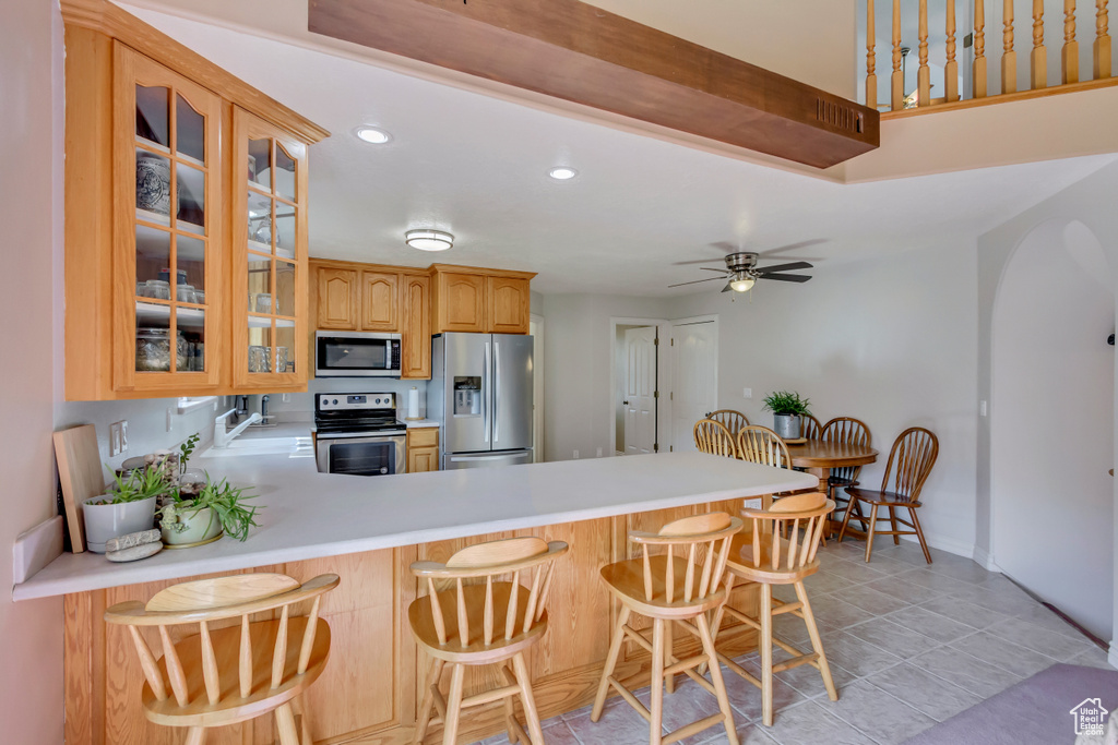 Kitchen with recessed lighting, glass insert cabinets, appliances with stainless steel finishes, light countertops, and a peninsula