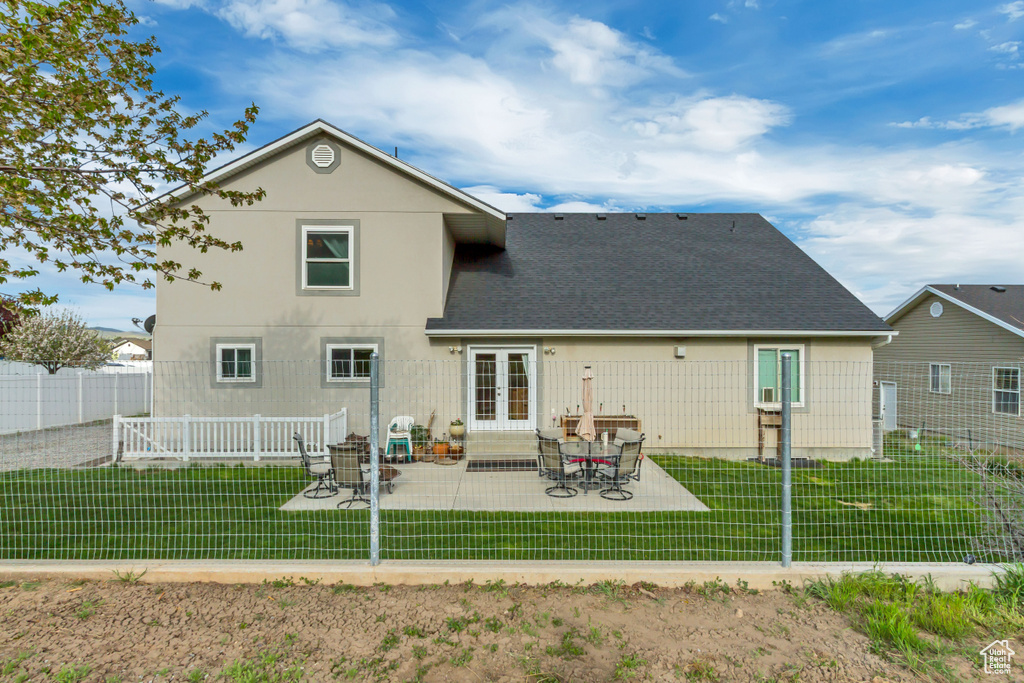Rear view of house with a patio, french doors, roof with shingles, and a lawn