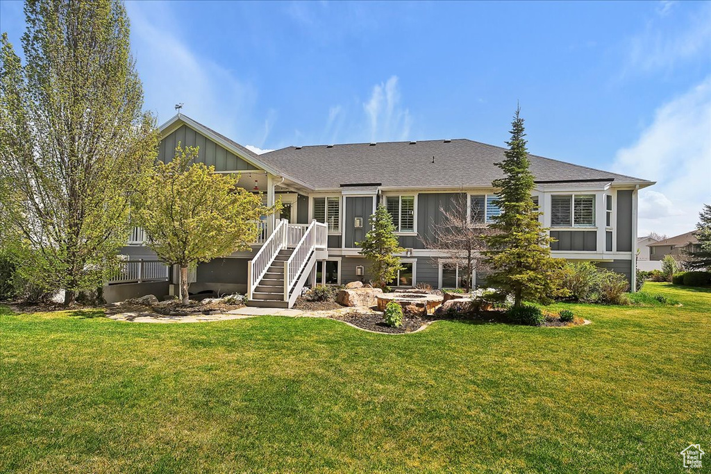 Rear view of house with a deck, board and batten siding, stairs, roof with shingles, and a lawn