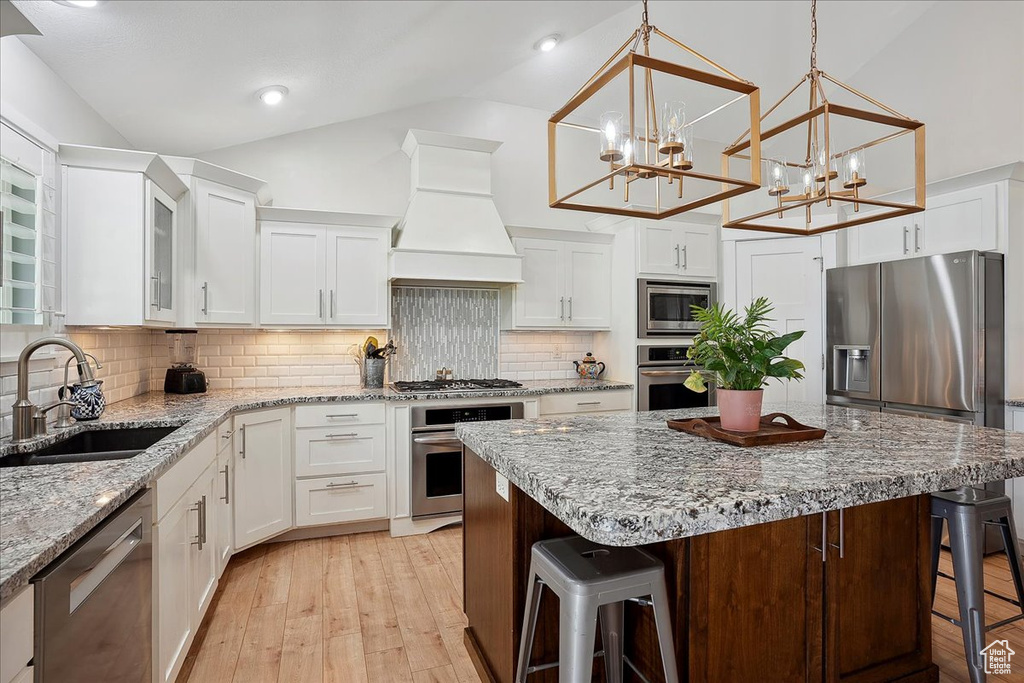 Kitchen featuring stainless steel appliances, a sink, a kitchen breakfast bar, lofted ceiling, and premium range hood